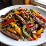 Close-up of perfectly cooked steak fajitas with colorful peppers and onions on a white plate.
