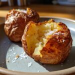 Close-up of a fluffy air fryer baked potato, split open and topped with coarse sea salt.