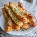 A stack of freshly baked, golden brown breadsticks generously topped with grated Parmesan cheese and chopped parsley.