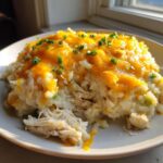 A close-up serving of cheesy chicken and rice topped with melted orange cheddar cheese and chopped green onions.