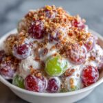 A close-up of a creamy grape salad, featuring red and green grapes coated in dressing and topped with crunchy pecans, resembling the Chicken Salad Chick grape salad.