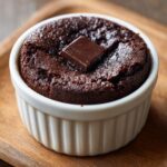A fudgy Cottage Cheese Microwave Brownie served hot in a white fluted ramekin, topped with a square of melting dark chocolate.