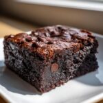 A close-up of a fudgy sweet potato brownies square topped with melted chocolate chips on a white plate.