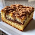 A close-up photo of a moist slice of coffee cake featuring a thick cinnamon swirl and generous crumb topping.