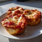 Three freshly baked pizza muffins topped with bubbling tomato sauce and melted mozzarella cheese, served on a white plate.