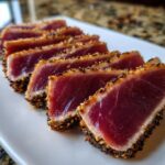 Slices of perfectly seared ahi tuna, crusted with black and white sesame seeds, showing a rare, deep red center.
