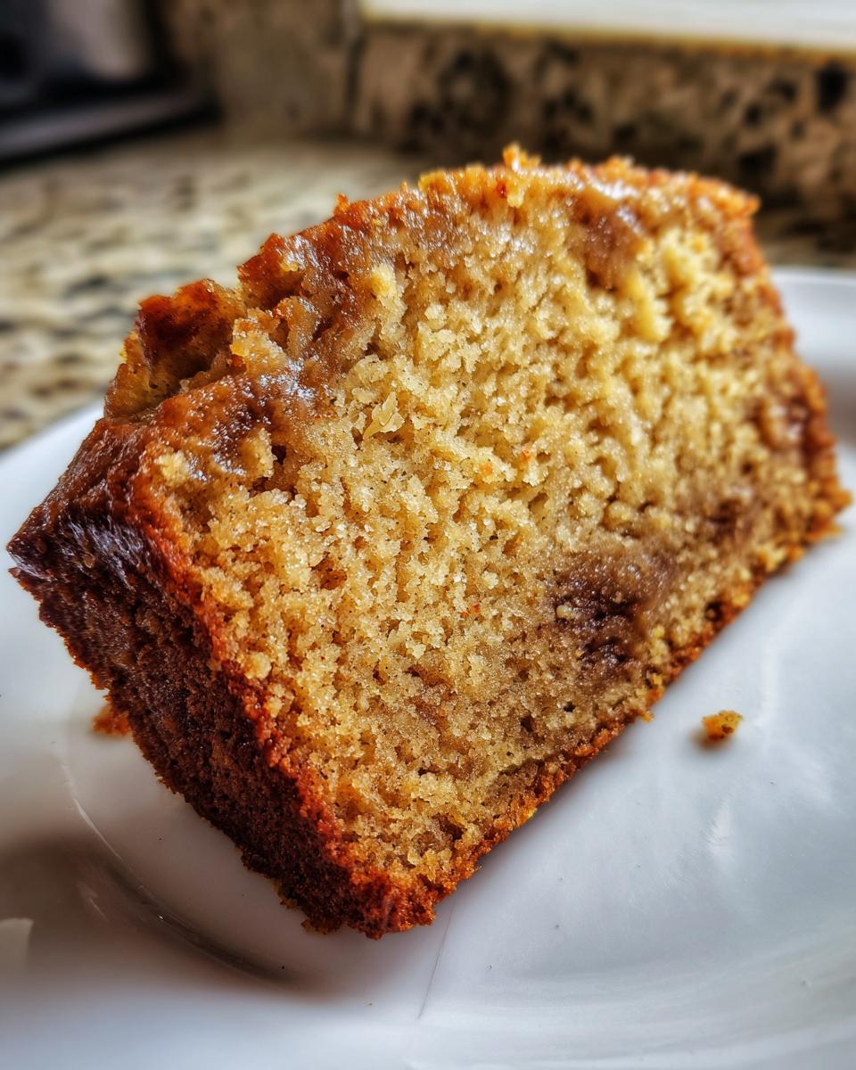Close-up of a moist, golden slice of sugar free banana bread resting on a white plate.