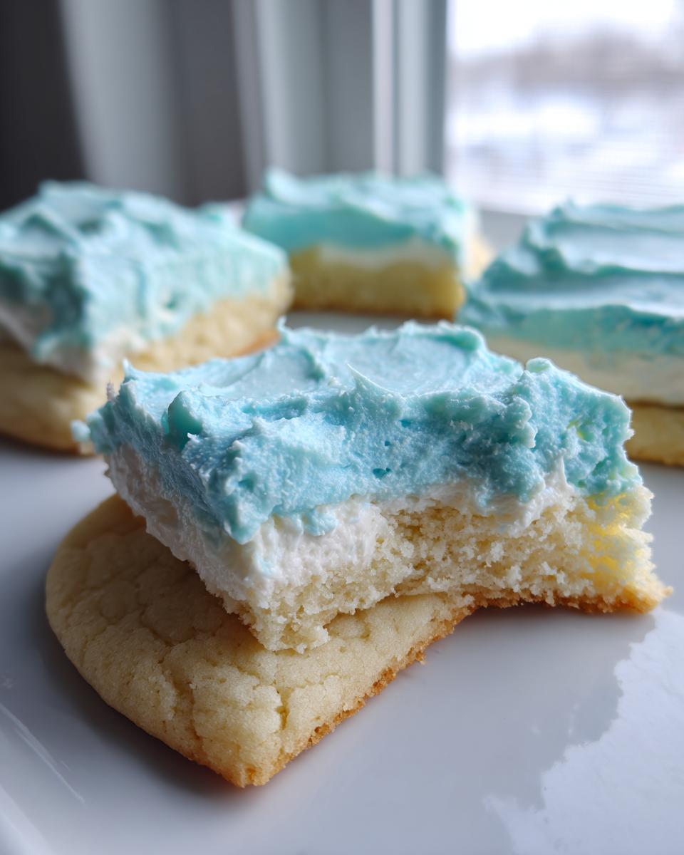 A bite taken out of a thick, frosted sugar cookie square showing the soft interior and bright blue frosting.