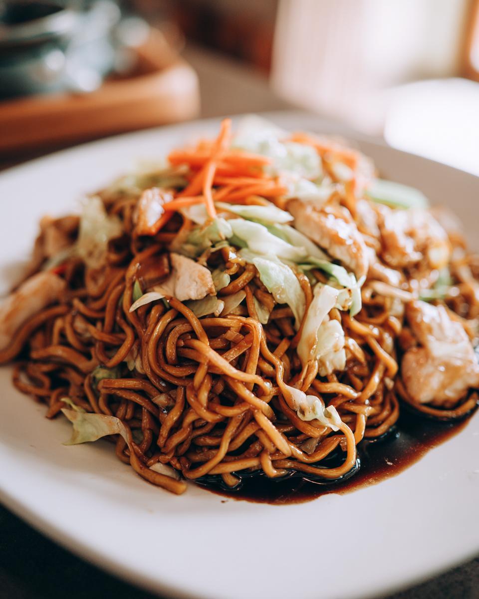 Close-up of a plate featuring a generous serving of chicken chow mein recipe with noodles, chicken pieces, cabbage, and shredded carrots.