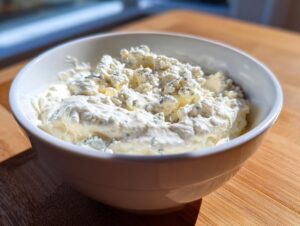 Close-up of chunky, creamy blue cheese dip topped with crumbles of blue cheese in a white bowl.