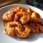 A close-up of perfectly cooked air fryer frozen shrimp, seasoned with spices, piled on a white plate.