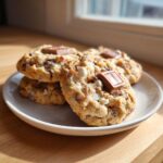 A stack of three delicious almond joy cookies topped with milk chocolate squares, sitting on a white plate.