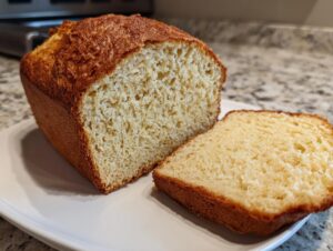 A golden-crusted loaf of homemade beer bread, partially sliced, resting on a white plate.