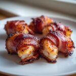 Close-up of several perfectly cooked bacon wrapped shrimp on a white plate, showing crispy, caramelized bacon.