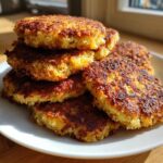 A stack of perfectly golden brown, crispy fried cornbread patties piled high on a white plate.