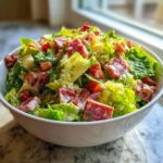 A close-up of a vibrant grinder salad featuring chopped romaine lettuce, chunks of salami, and creamy dressing in a white bowl.