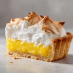 Close-up of a slice of amazing lemon pie showing bright yellow filling, flaky crust, and toasted meringue topping.