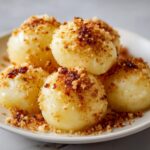 A plate of freshly made potato dumplings topped generously with sweet, browned breadcrumbs.