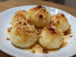Close-up of four perfectly rounded potato dumplings coated in toasted brown sugar crumbs.