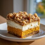 A perfect square slice of pumpkin crunch dessert with a crust, creamy layer, and crumb topping.
