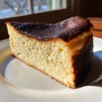 A close-up slice of creamy Basque cheesecake showing its signature dark, caramelized top.