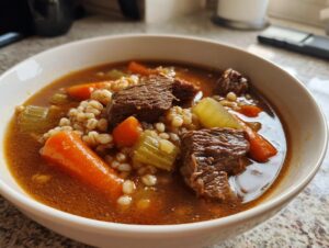 Close-up of a hearty bowl of beef barley soup featuring tender beef chunks, carrots, celery, and barley in a rich broth.