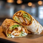 Close-up of a perfectly grilled buffalo chicken wrap cut in half, showing spicy chicken, lettuce, and creamy sauce.