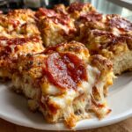 Close-up of a gooey slice of pepperoni pizza casserole being pulled away, showing melted cheese strings.