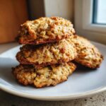 A stack of three golden brown, chewy banana oatmeal cookies piled on a light plate near a window.