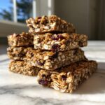 A stack of homemade no bake granola bars made with oats, dried cranberries, and chocolate chips, resting on a marble surface.