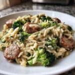 A close-up of creamy chicken sausage and broccoli orzo served in a white bowl.
