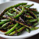 A close-up of vibrant green beans coated in a dark, savory garlic sauce, ready to eat.