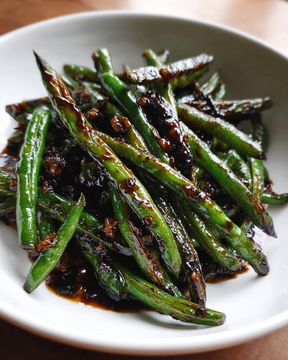 Close-up of vibrant chinese green beans with garlic sauce, glistening in a white bowl.