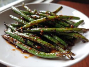 Close-up of vibrant green beans coated in a glossy, dark garlic sauce, ready to serve.