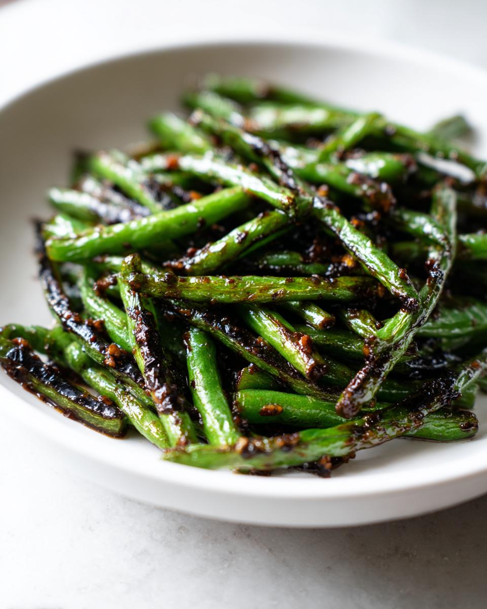 Close-up of vibrant green beans coated in a dark, savory garlic sauce, ready to serve.