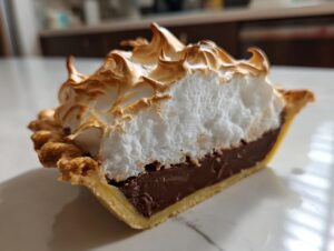 A close-up cross-section of a perfect chocolate meringue pie showing the crust, rich chocolate filling, and toasted meringue topping.