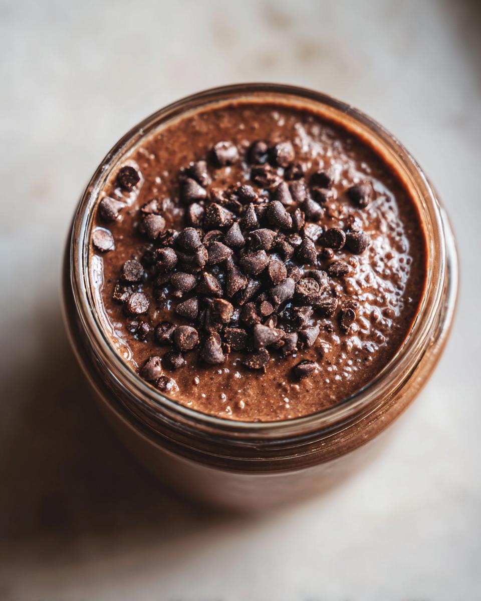 Overhead view of rich chocolate overnight oats in a glass jar, generously topped with mini chocolate chips.