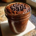 Close-up of rich chocolate overnight oats topped with mini chocolate chips in a glass jar.