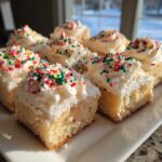 Several squares of fluffy Christmas sugar cookie bars topped with white frosting and festive red, green, and white sprinkles.