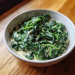 A close-up of a rustic bowl filled with vibrant green creamed spinach recipe, sitting on a wooden table.