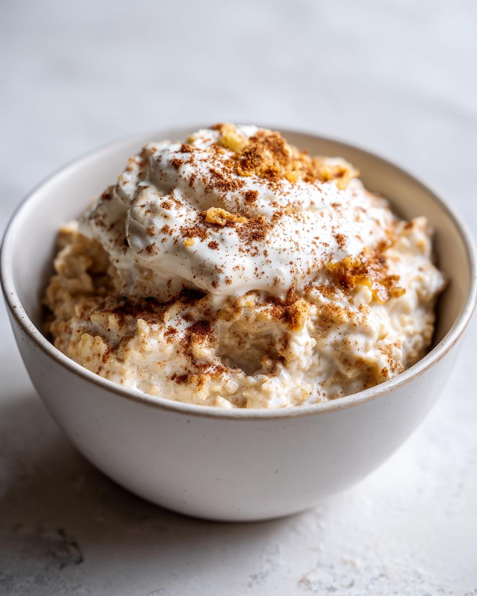 A close-up of creamy banana oatmeal in a white bowl, topped with yogurt, cinnamon, and nuts.