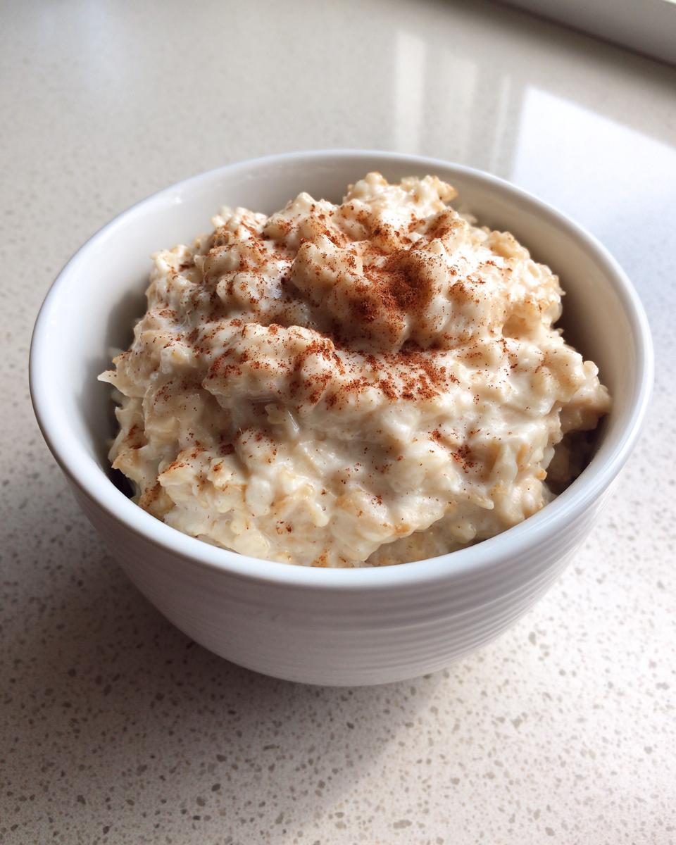A white bowl filled with creamy banana oatmeal, topped generously with sprinkled cinnamon.