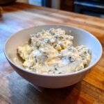 A close-up of a white bowl filled with chunky, creamy blue cheese dip mixture.