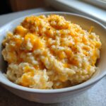 A close-up view of creamy cheesy rice topped with melted cheddar cheese and black pepper in a white bowl.