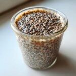 A close-up view of thick, creamy chia seed pudding soaking in milk inside a clear glass jar.
