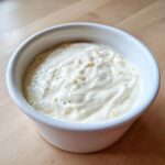 Close-up of thick, creamy garlic sauce with visible minced garlic pieces in a small white bowl.