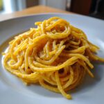 A close-up shot of perfectly twirled creamy lemon pasta coated in a rich, yellow sauce and sprinkled with black pepper.