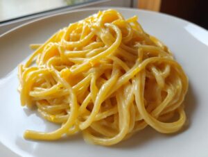 A close-up view of a serving of creamy lemon pasta, coated in a rich, yellow sauce, presented on a white plate.