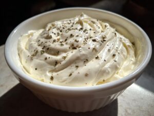 Close-up of thick, creamy olive garden alfredo sauce topped with dried herbs and pepper in a white bowl.