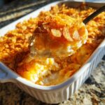 A spoonful of creamy potato casserole with a golden, crunchy topping being lifted from a white baking dish.